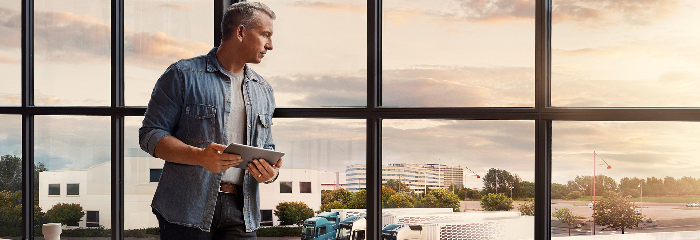Чоловік з планшетом стоїть біля вікна й дивиться униз на свій автопарк